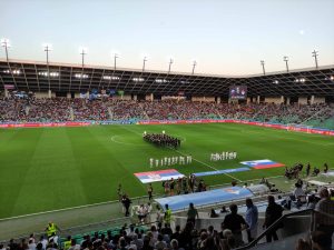 Nogometni stadion Stožice na zelenici sta razgrnjeni zastavi Slovenije in Srbije. V ozadju je orkester