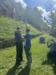 Fotografija udeleženca, ki ob pomoči trenerke strelja z lokom na tarčo