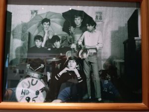 Na sliki je skupina 6 glasbenikov. Trije stojijo - 2 izmed njih imata odprt dežnik, eden ima v rokah tamburin. Tu sta še dva glasbenika, oba oblečena v črno - eden rahlo tolče s paličicami po bobnu, drugi ima v roki pokonci postavljeno kitaro. Šesti glasbenik je Andrej, ki rahlo zleknjen sedi v prvi vrsti in si z rokama podpira glavo.