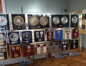 Na sliki je velika vitrina, v njej pa razstavljene plošče Andreja Šifrerja. Plošče so v različnih odtenkih glede na število prodanih izvodov.