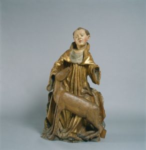 Lesen kip mlade osebe v pozlateni obleki, ki sedi ali kleči ter z roko nežno drži glavo košute, stoječe ob njenem naročju. Figuri delujeta mirno, postavljeni na nevtralnem sivem ozadju.